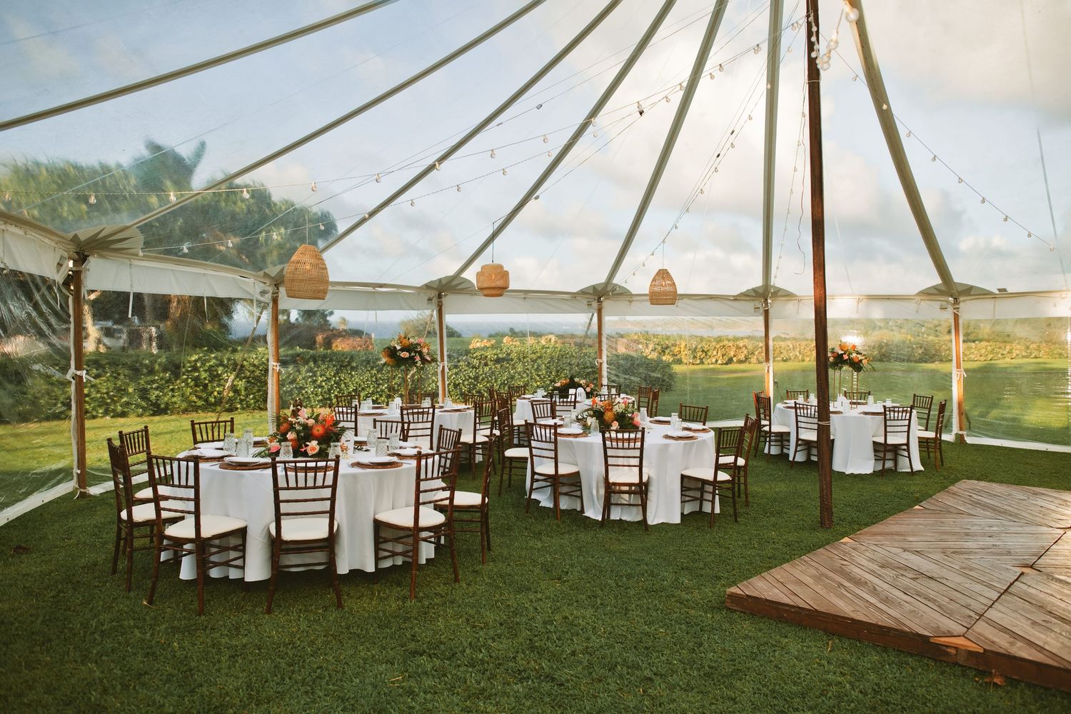Elegant outdoor wedding reception under a sailcloth tent with round tables and ocean views.
