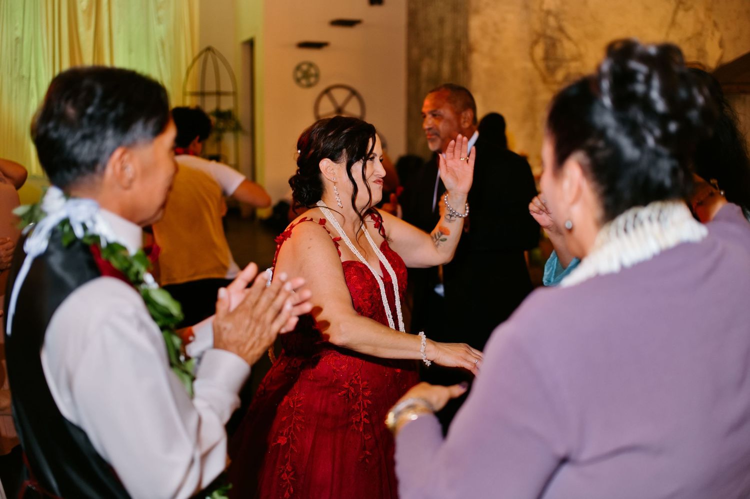 Woman in red dress dancing joyfully with guests at a festive celebration or wedding reception.
