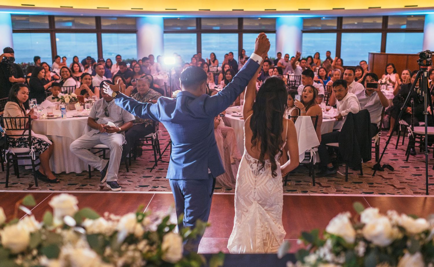 Wedding celebration in a spacious ballroom with decorative lighting and floral arrangements.