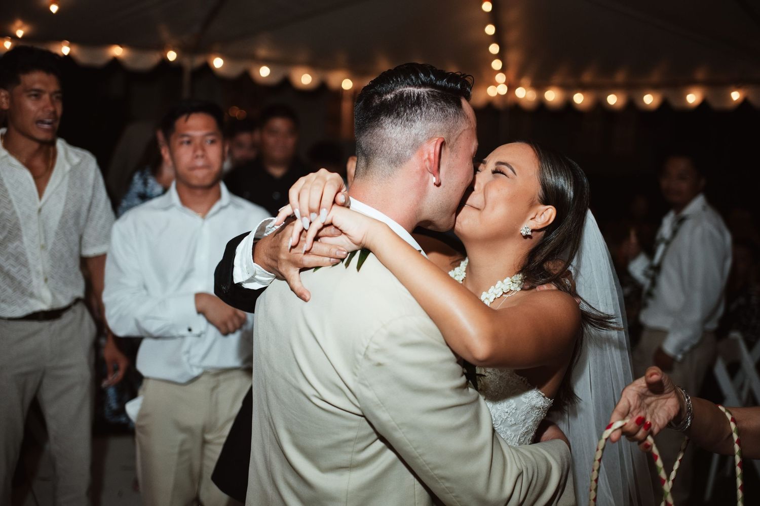 Bride and groom share first dance under string lights at outdoor wedding reception with guests watching.