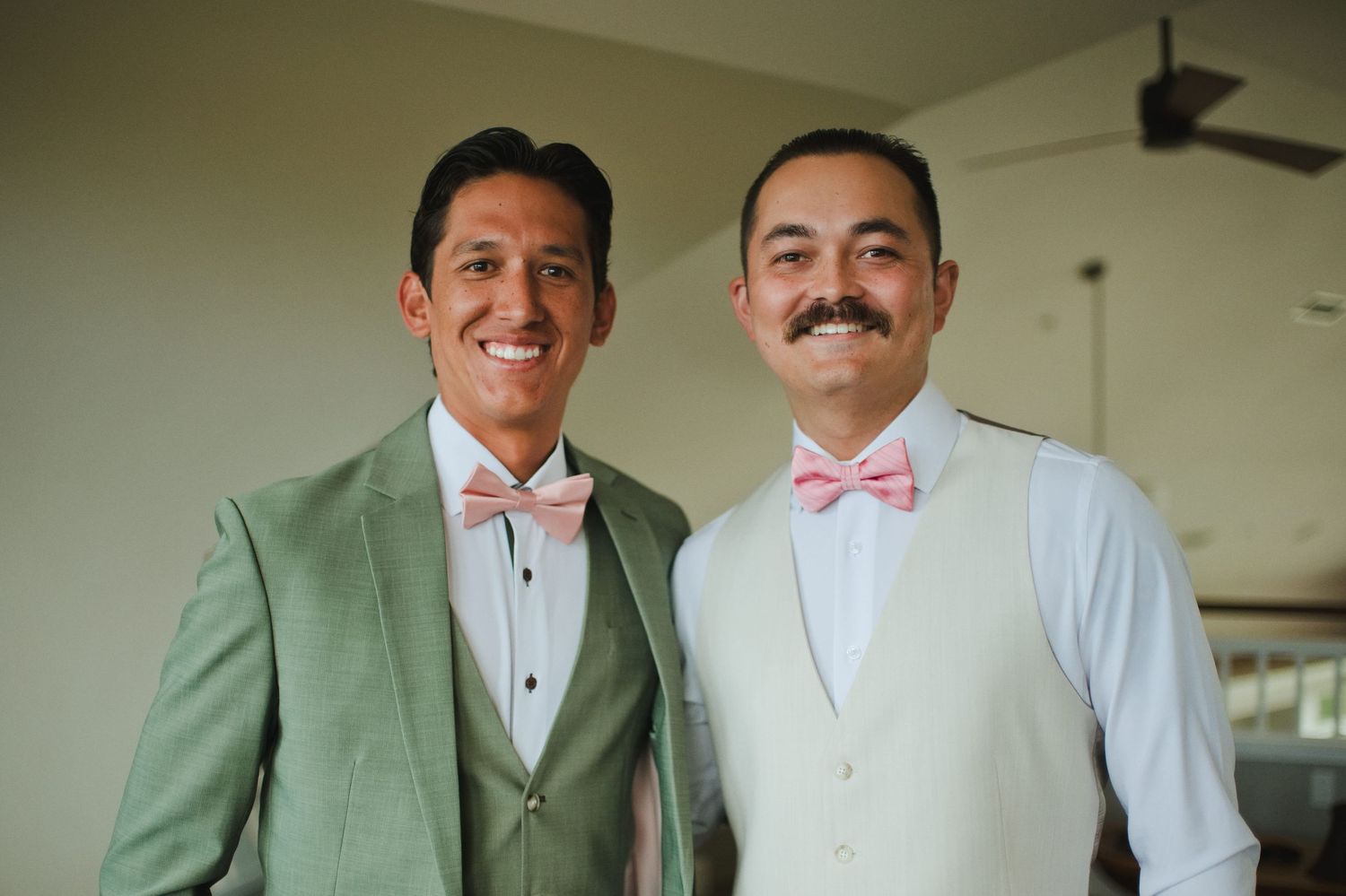 Two men in matching pink bow ties and formal attire smile together at a wedding celebration.