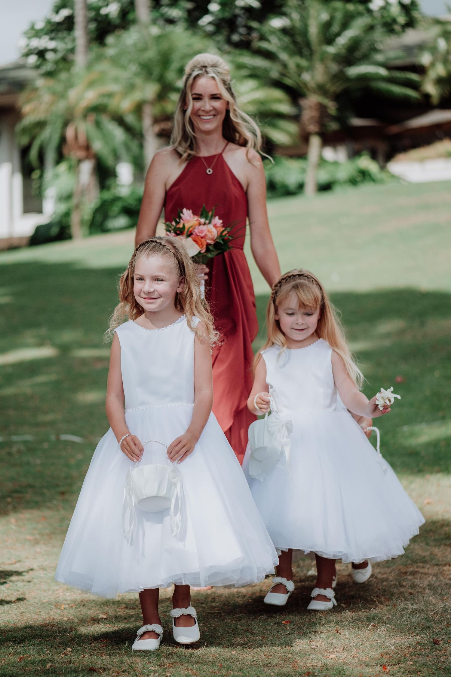 Flower girls in white tulle dresses walk down grassy aisle at outdoor wedding.
