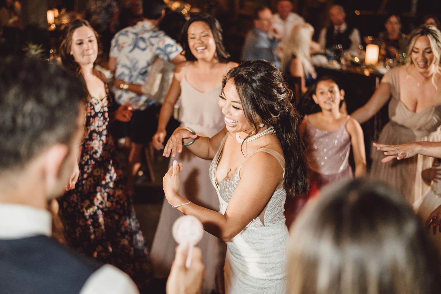 Wedding guests dancing and celebrating during reception party under ambient lighting.