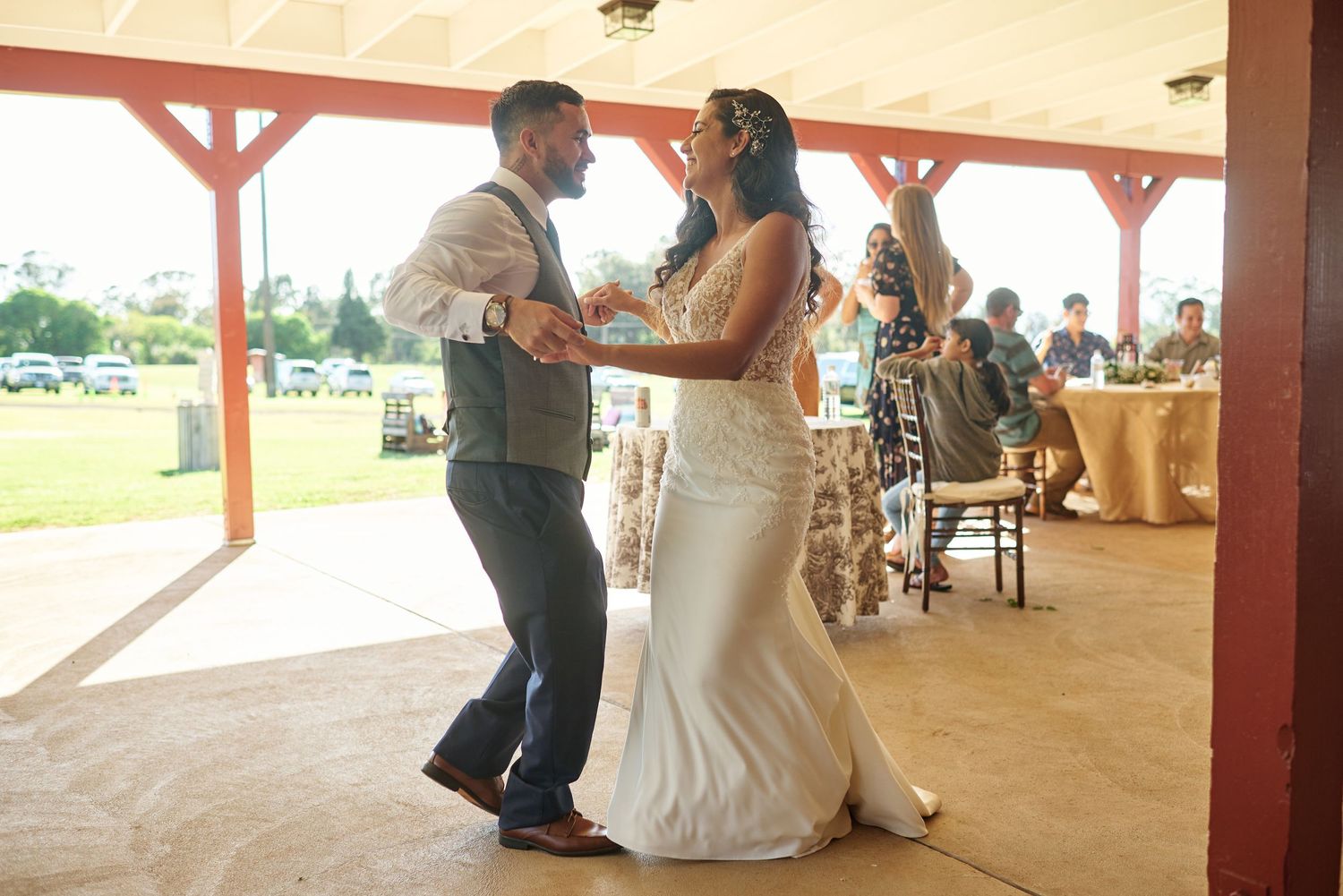 Dancing couple celebrates during wedding reception in covered outdoor pavilion.