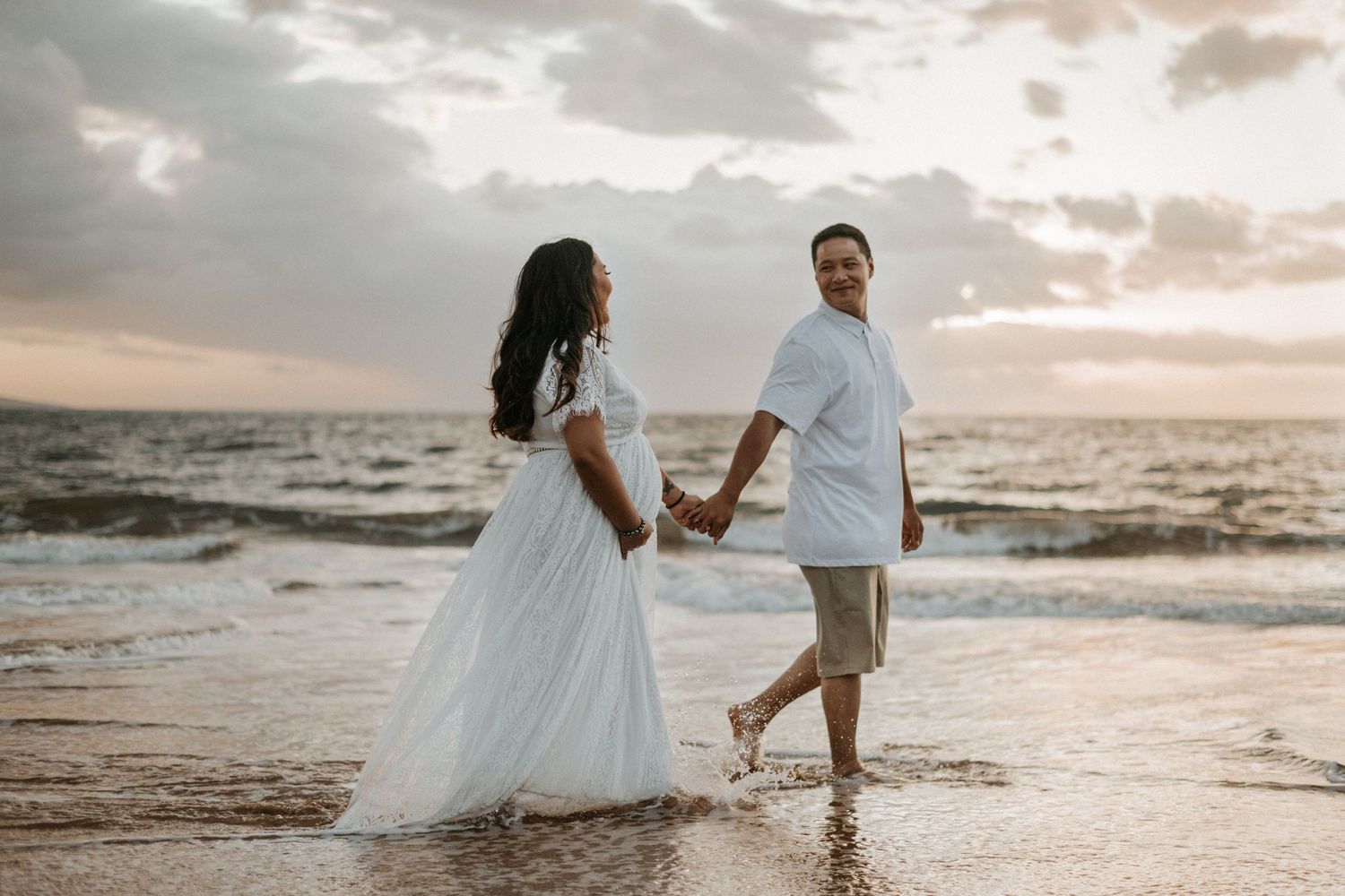 Couple walking through ocean waves during golden hour beach photo session.