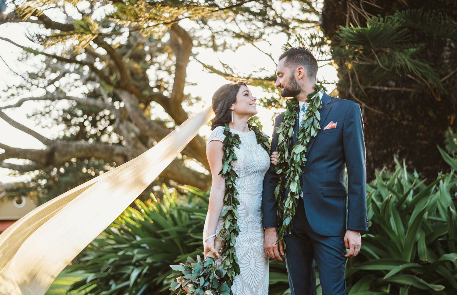 Romantic wedding portraits captured through garden foliage during golden hour.