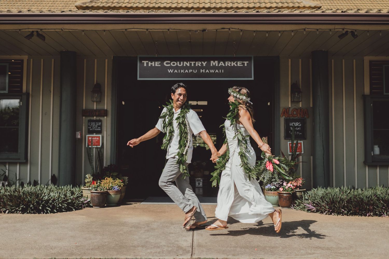 Couple in floral leis holding hands outside The Country Market in Waikapu, Hawaii, celebrating their wedding day.