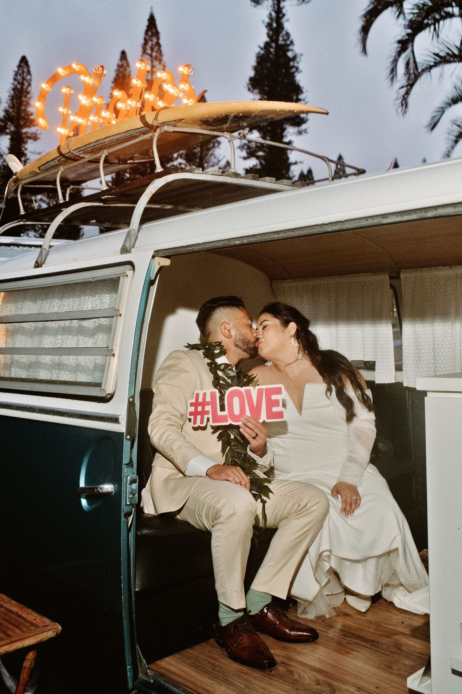 Bride and groom kissing inside a vintage VW camper van holding a #LOVE sign at their wedding.