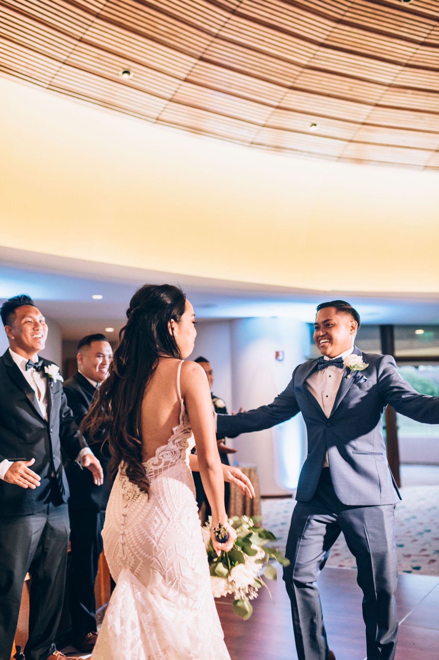Wedding party members dance in formation wearing formal attire in modern reception venue.