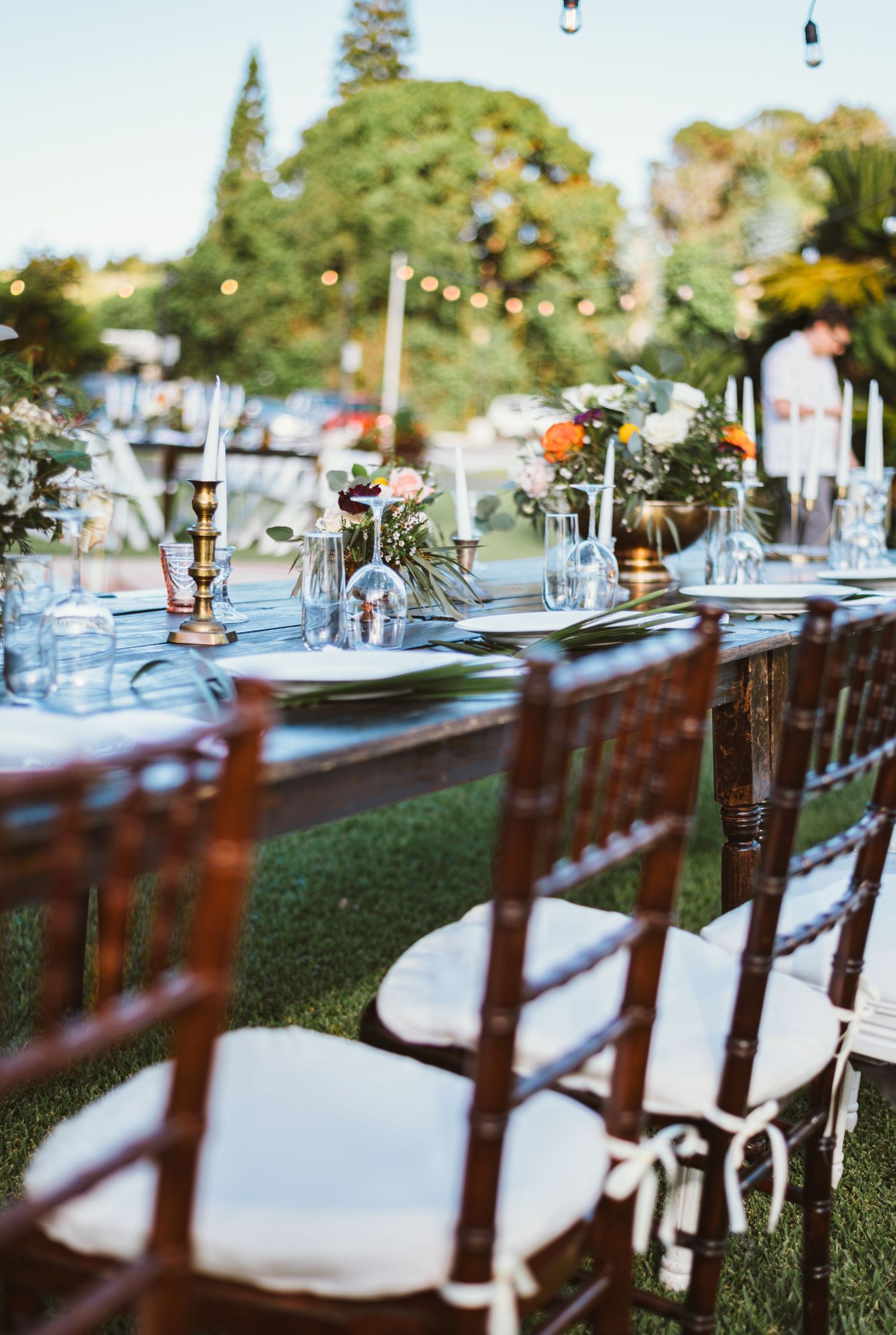 Long reception tables with white chairs set up outdoors for a garden wedding.