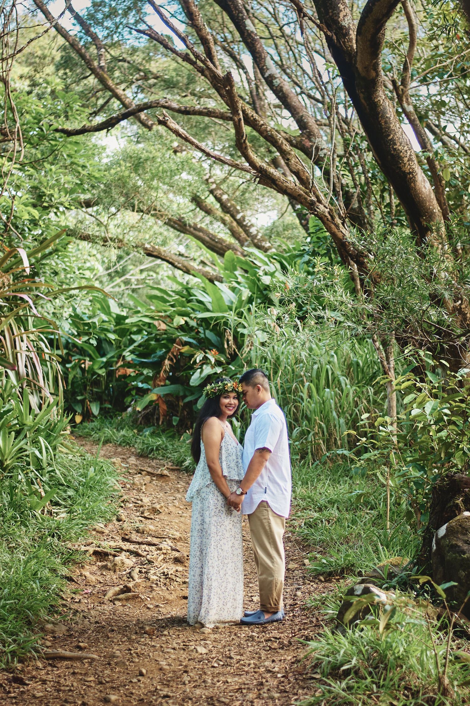 A couple walks hand in hand along a scenic forest trail surrounded by lush greenery.