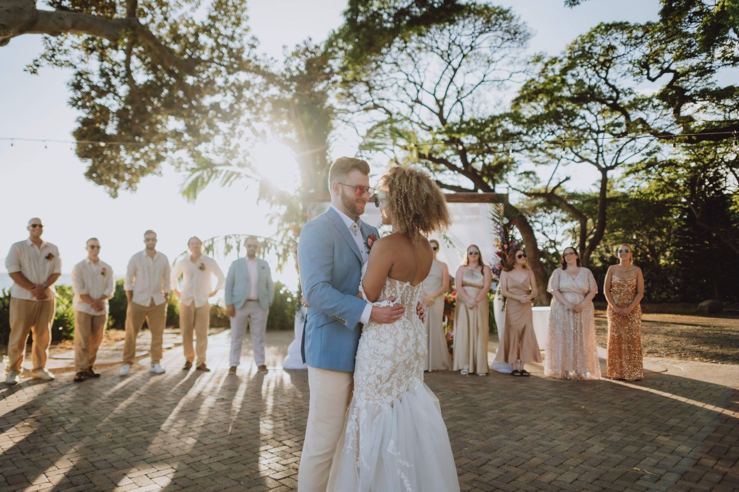 Wedding party lined up during golden hour with sun flare and trees in the background.