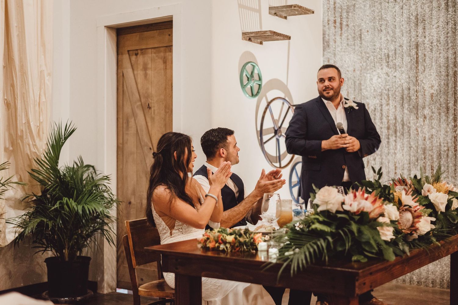 Wedding guests gathered around wooden tables during reception toasts and speeches.