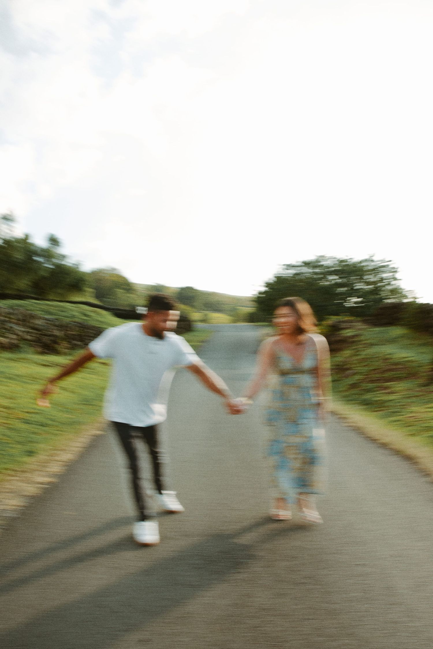 Blurred motion photo of a couple holding hands walking down a scenic road.