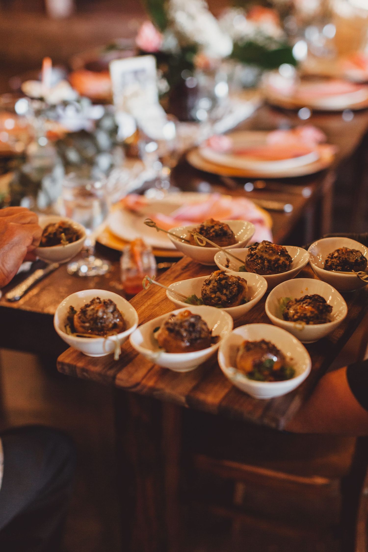 Elegant wedding reception table with small white bowls of appetizers on rustic wood, pink plates, and glassware.