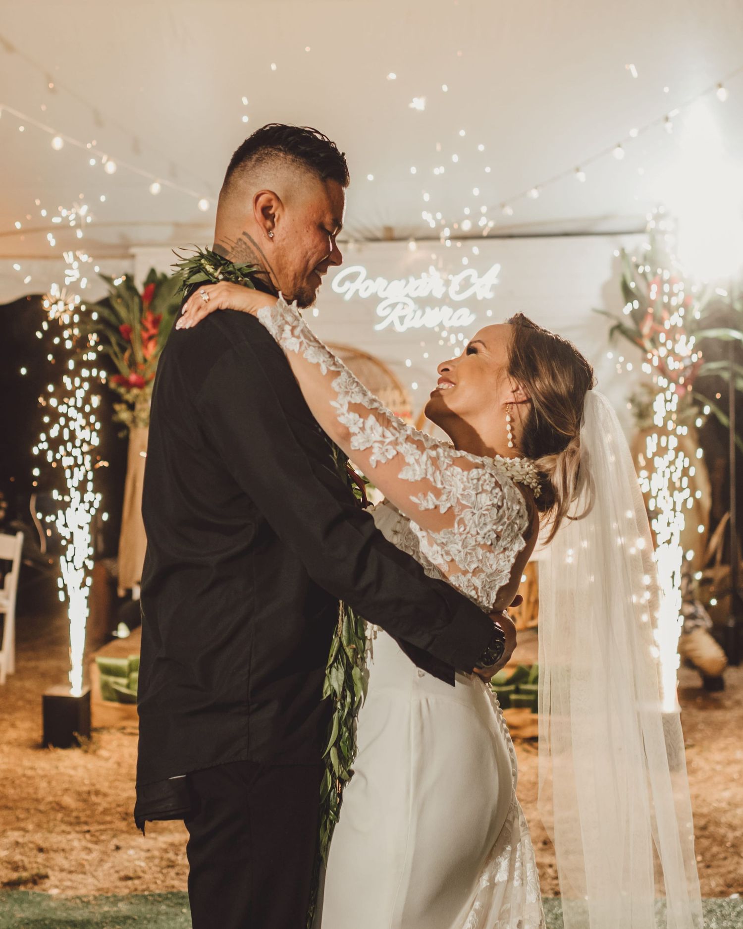 Bride and groom sharing a romantic first dance under sparkling lights with a neon Forever At Home sign at their wedding reception.