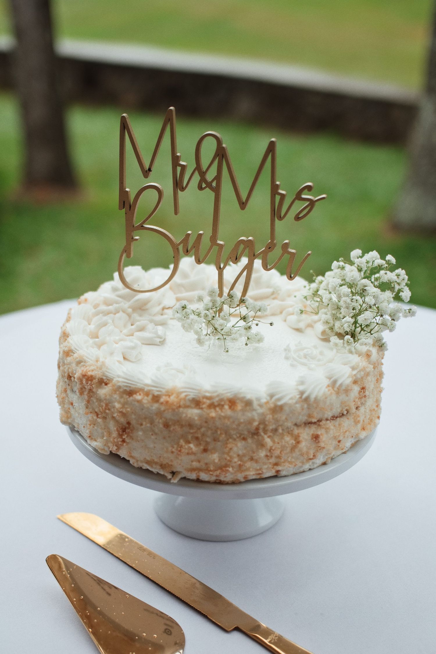 Elegant wedding cake with Mr & Mrs Burger gold topper and baby's breath flowers on white pedestal stand.