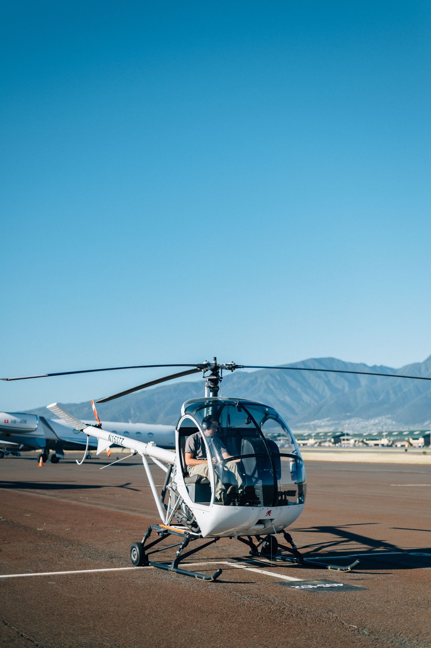 Multiple helicopters parked on desert airfield under bright blue sky.