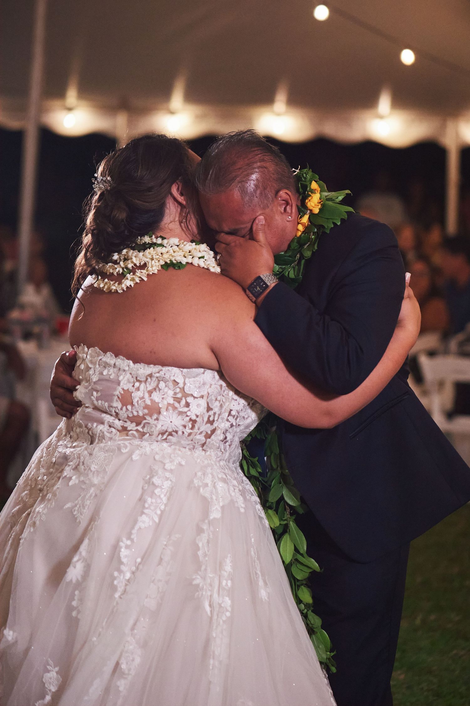 A romantic first dance between newlyweds wearing traditional Hawaiian leis under a tent.