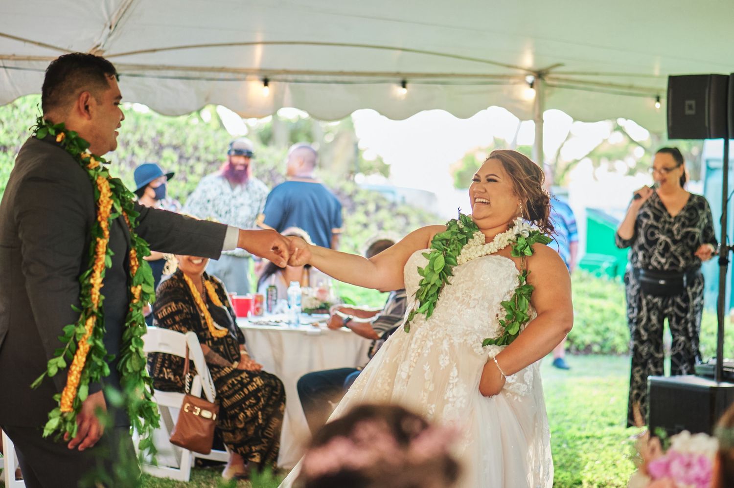 A couple wearing traditional Hawaiian leis dances at their wedding reception under a white tent.