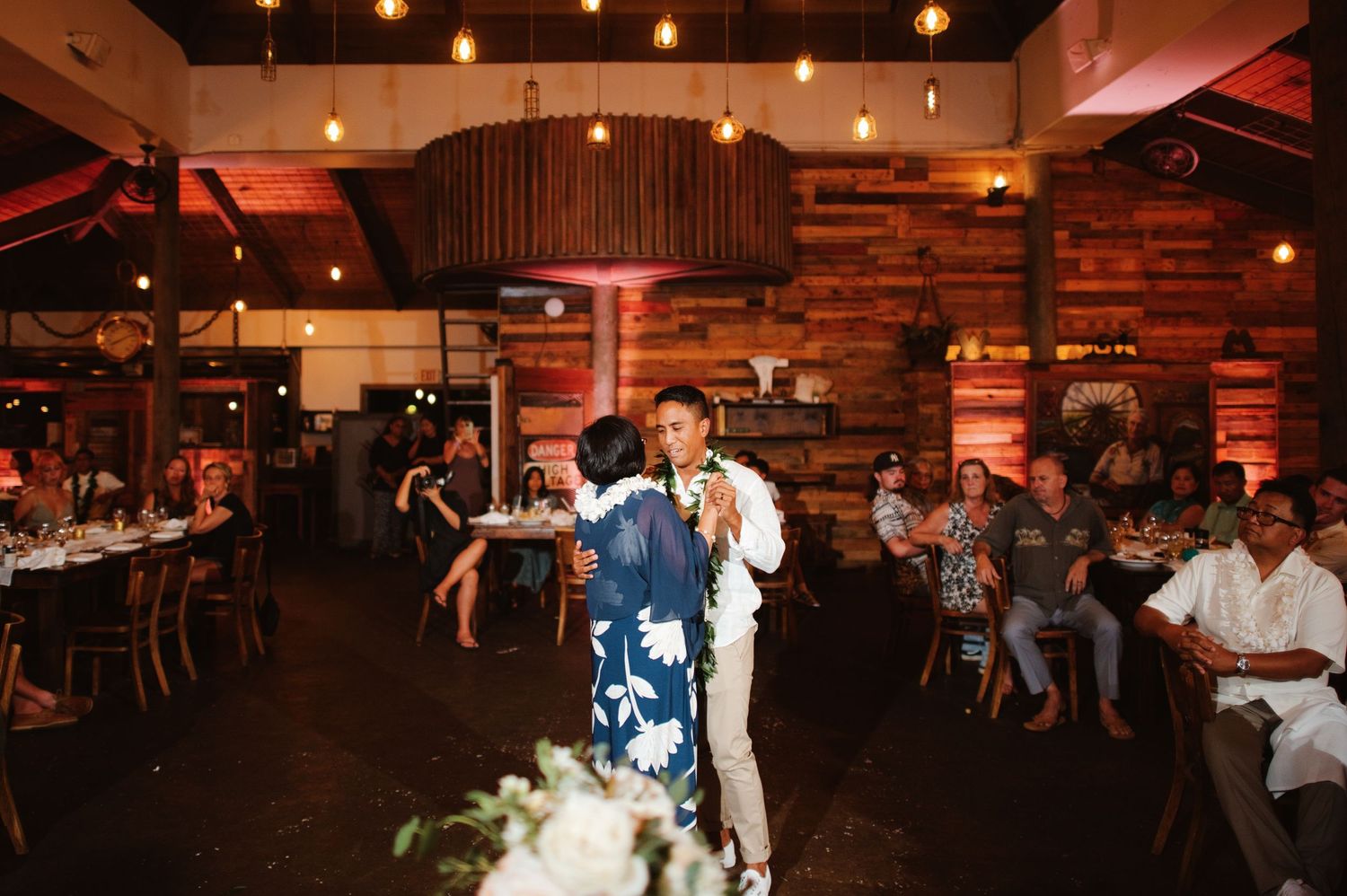Couple shares first dance at rustic wedding reception with warm Edison bulb lighting and wood plank walls.