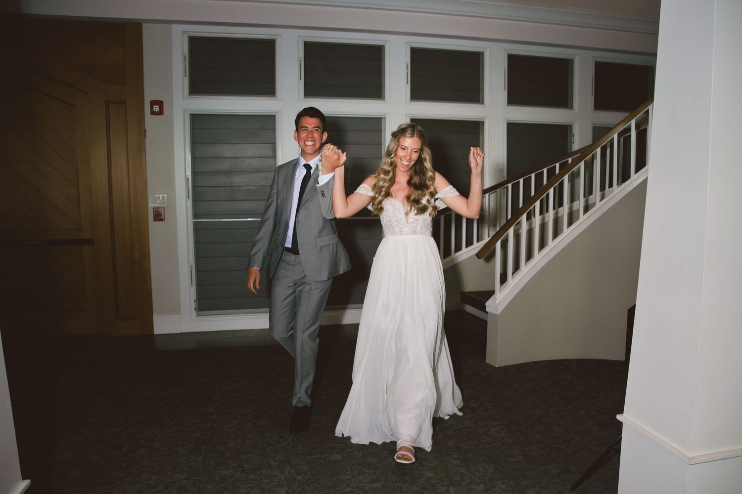 Bride and groom make grand entrance at wedding reception, bride in flowing white gown with floral crown, groom in gray suit.