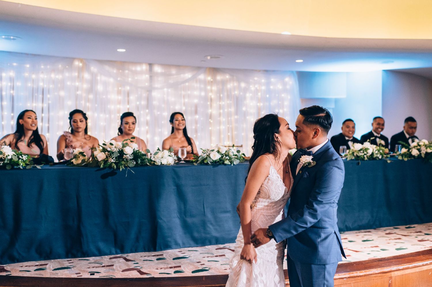 Wedding guests watch a couple dance in a modern reception venue with ambient lighting.
