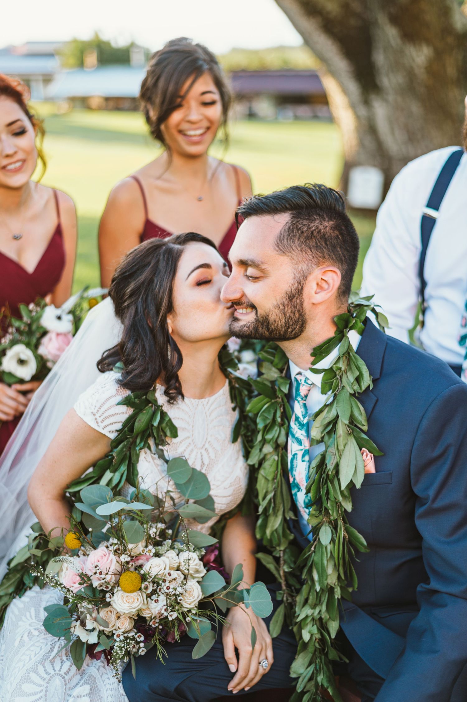 Wedding party wearing burgundy and navy poses together with greenery garlands and bouquets.