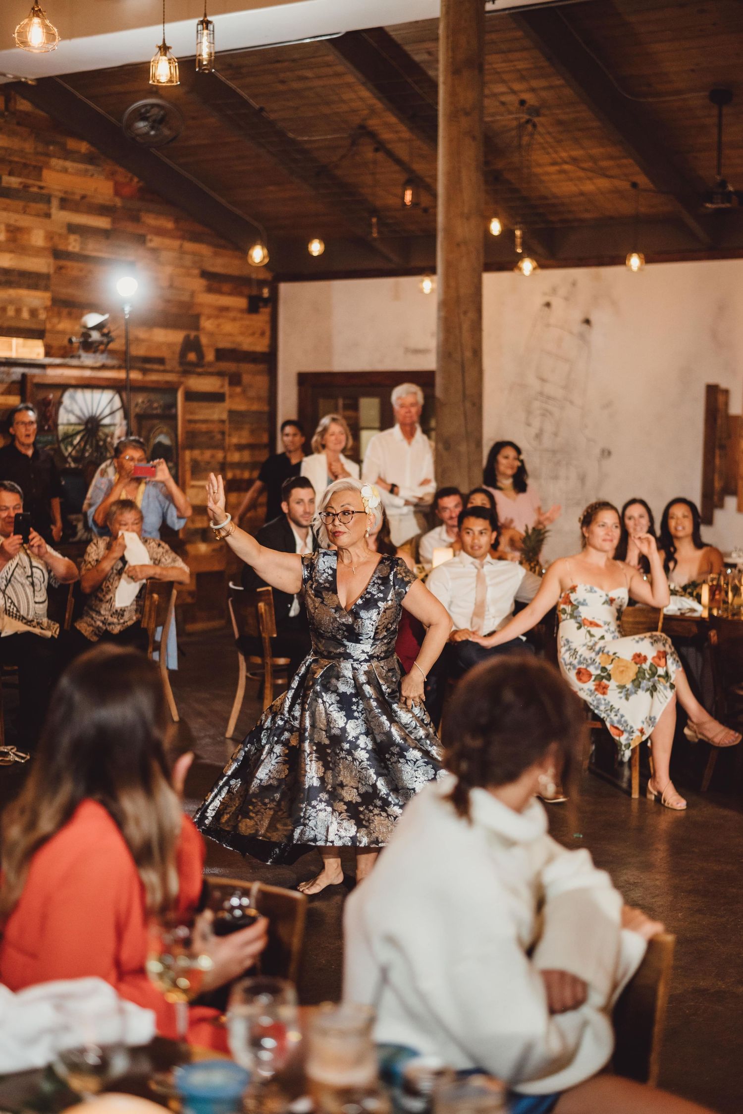 Wedding guests dancing and celebrating on wooden dance floor under string lights.