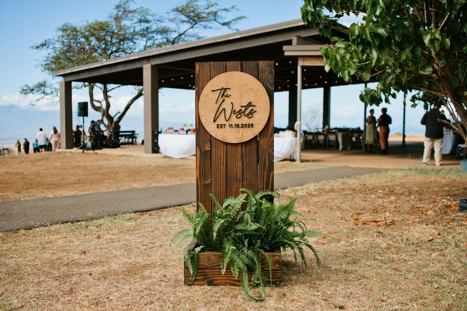 Rustic wooden wedding sign for The Wrights displayed outdoors near a tropical beach pavilion with lush ferns.