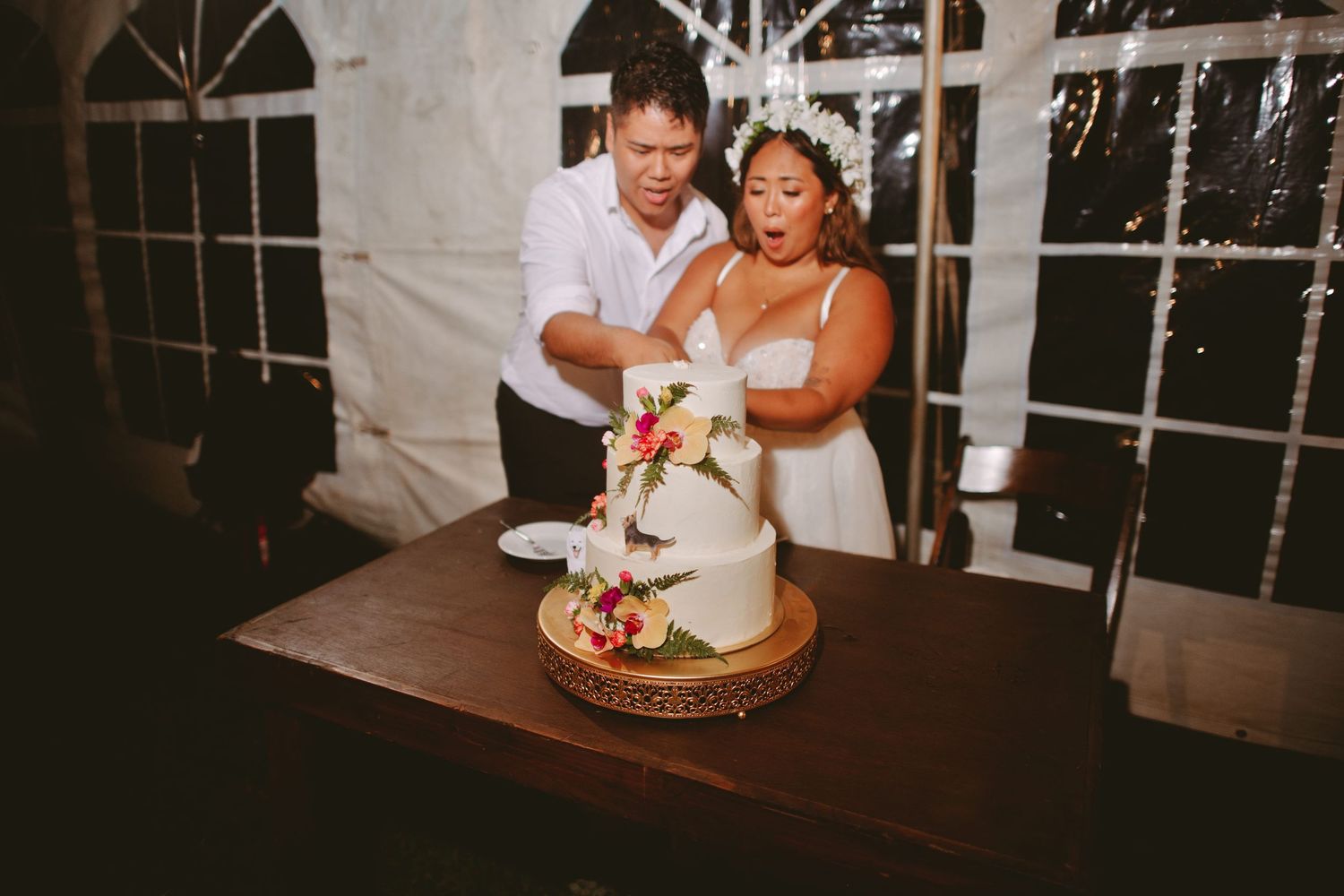 Bride and groom cutting their white wedding cake decorated with colorful flowers at a tented reception.