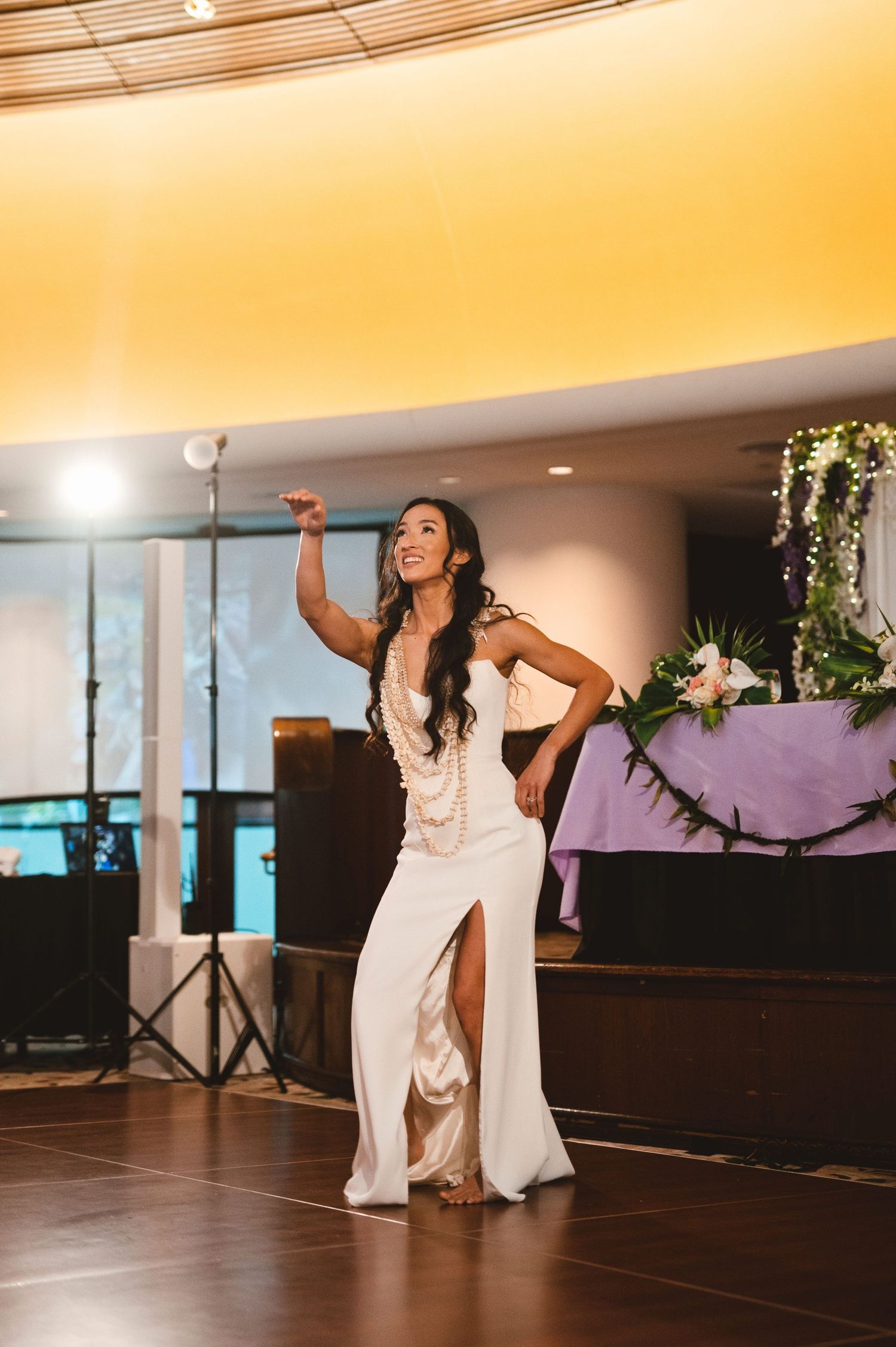 Bride in white gown with slit dances elegantly at wedding reception, smiling with arm raised.