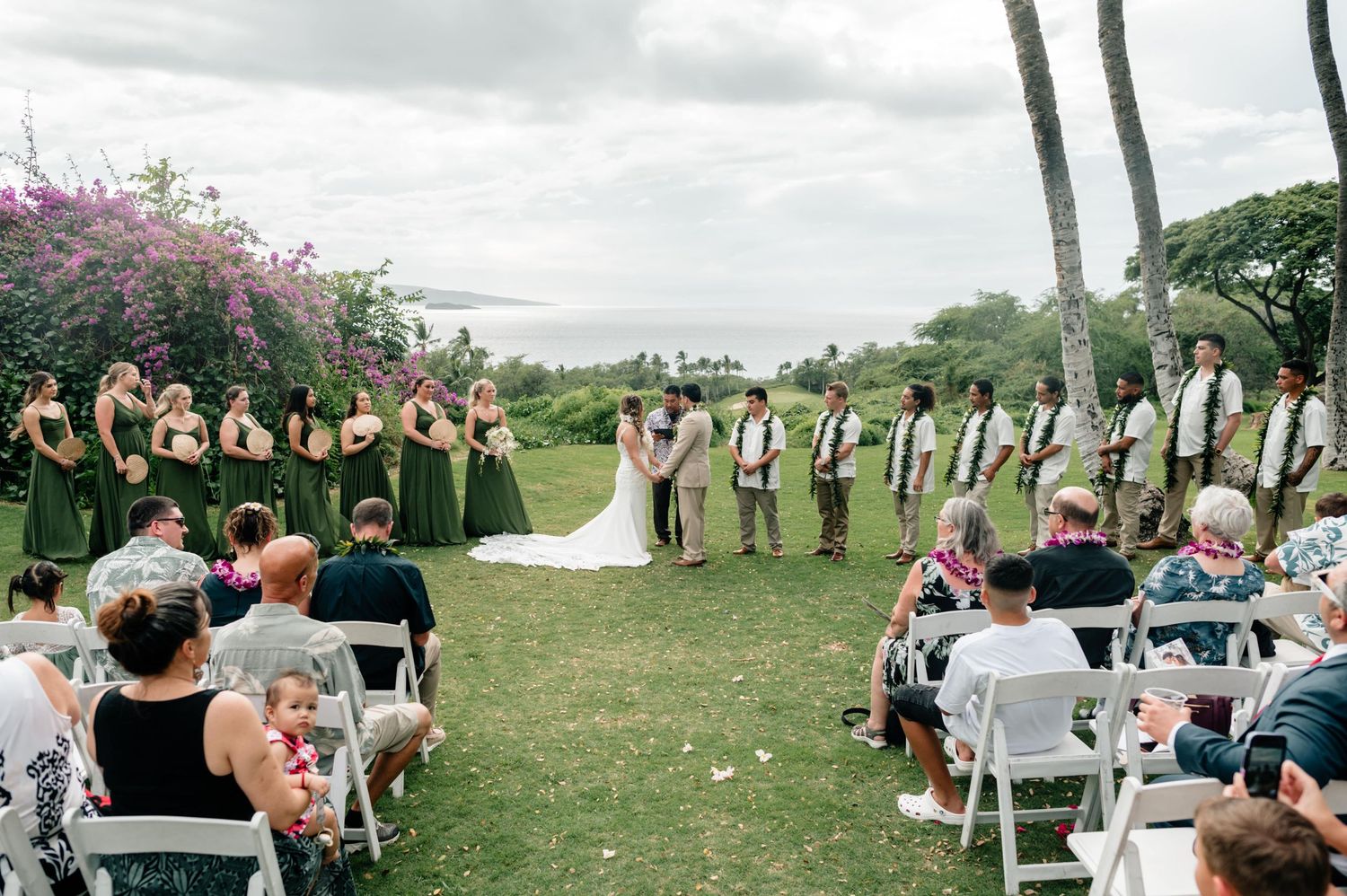 Outdoor wedding ceremony setup with white chairs and tropical landscape backdrop.