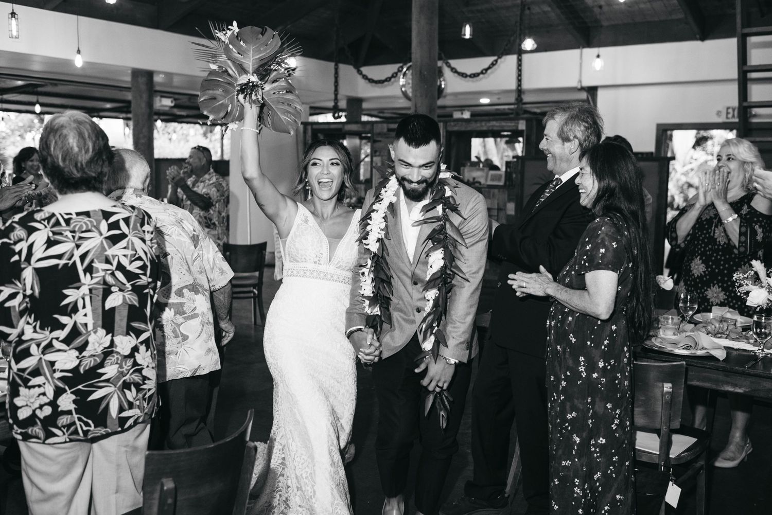 Black and white photo of newlyweds celebrating their wedding reception exit, bride holding bouquet aloft.