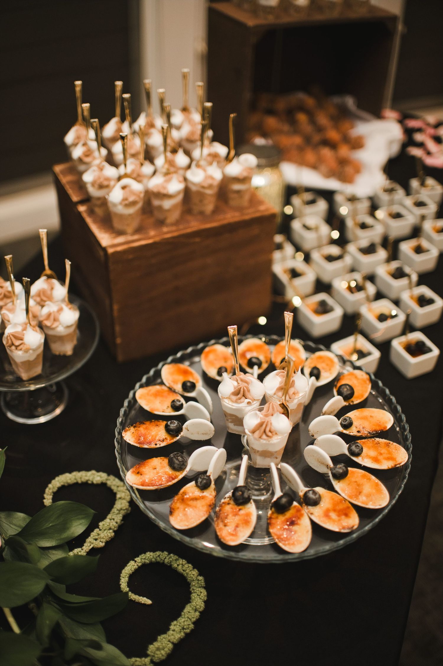Elegant catering display with brulee desserts, mini cups, and bite-sized appetizers arranged on a dark buffet table.