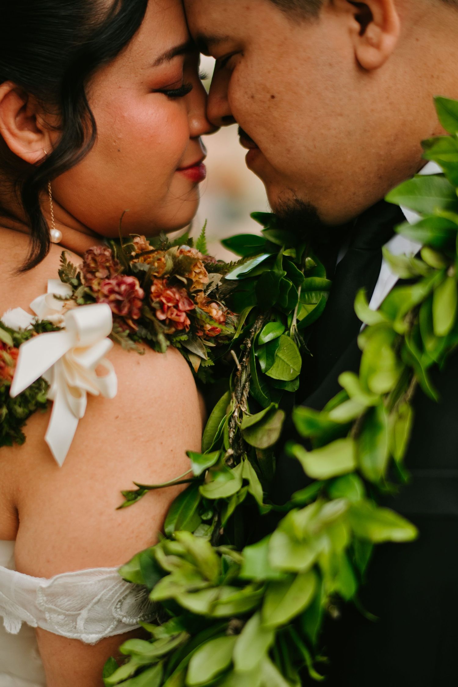 Bride and groom in Hawaiian lei touch foreheads in an intimate wedding moment.