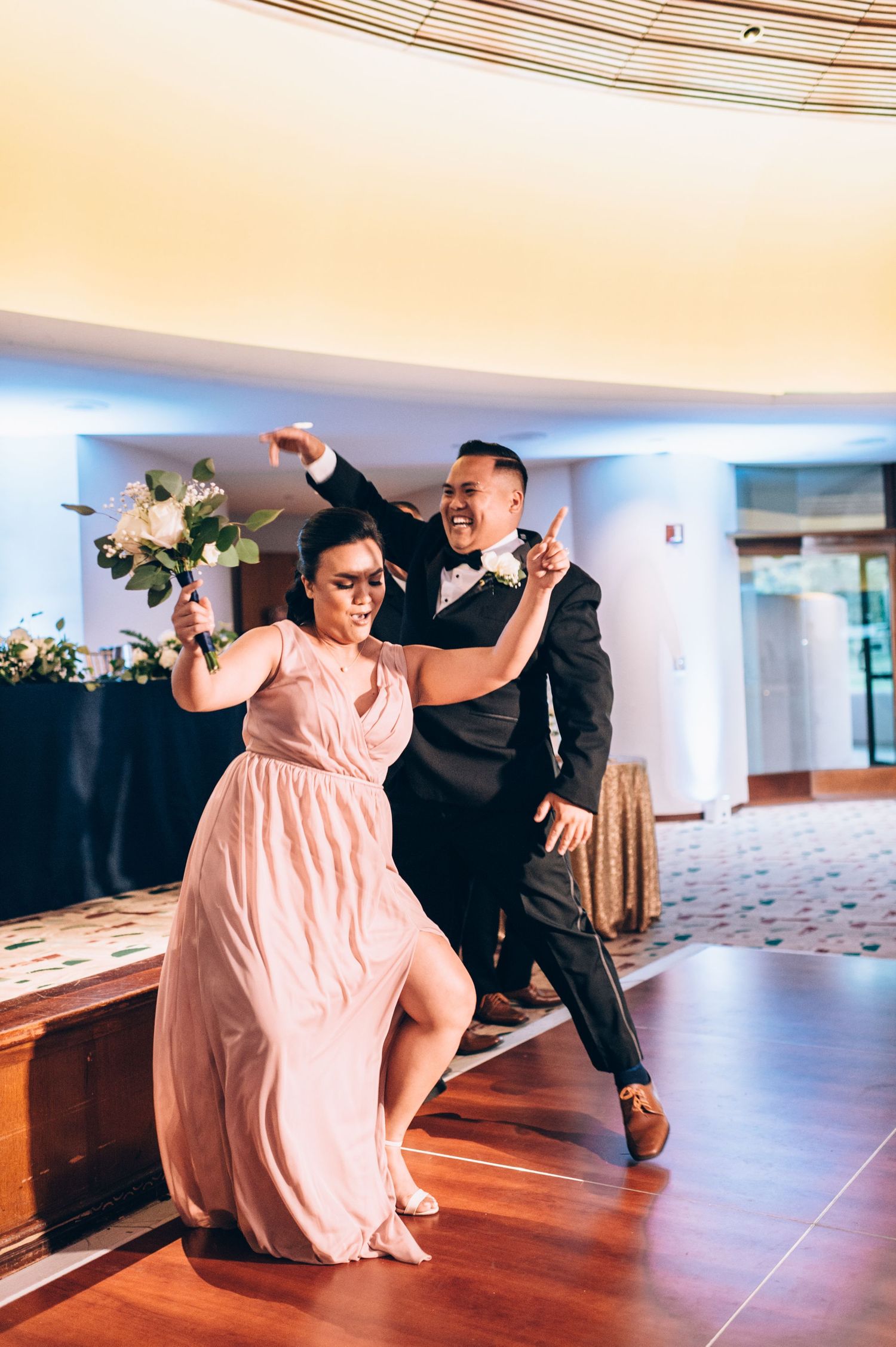 Wedding dancers execute a dramatic choreographed move in a modern venue with pink and black attire.