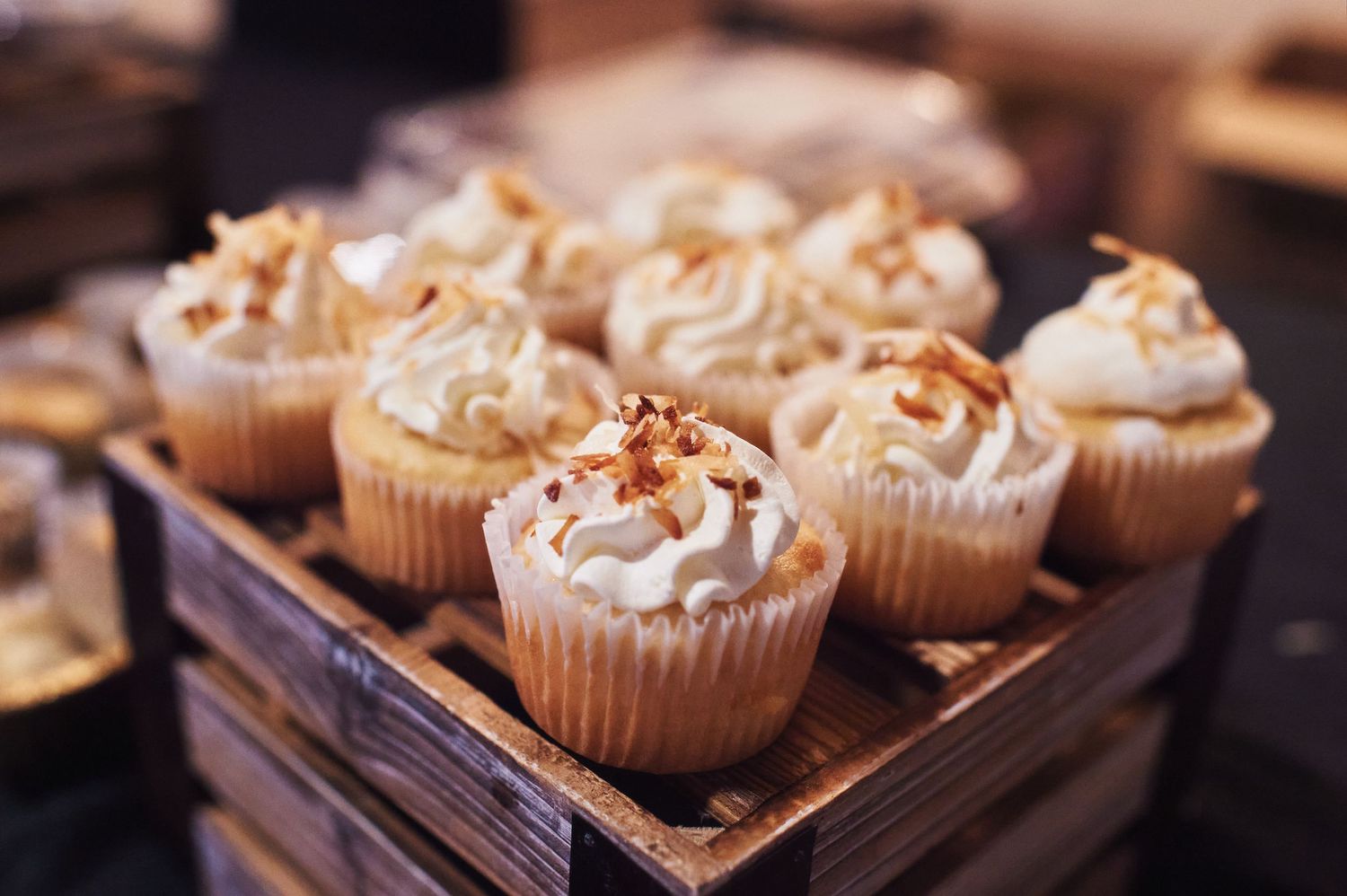 Frosted cupcakes with sprinkles displayed in a wooden box at a wedding dessert table.