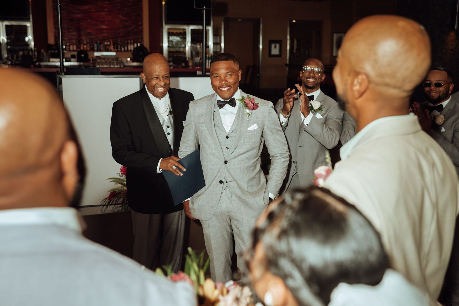 Groom in gray suit shaking hands with guest at wedding reception venue.
