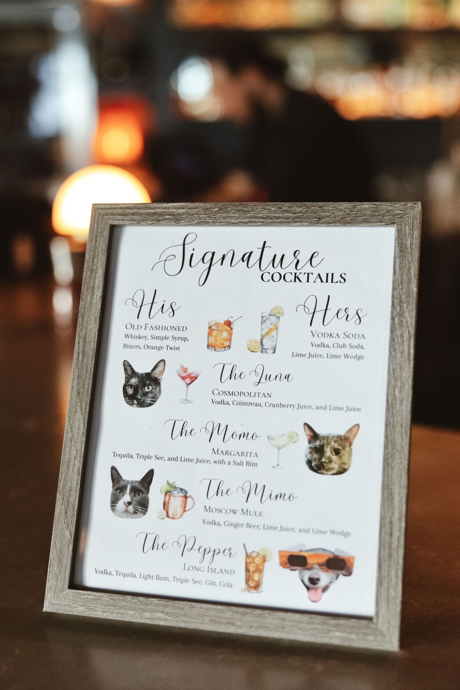 Framed signature cocktails menu with watercolor cat illustrations displayed on a bar for a wedding reception.