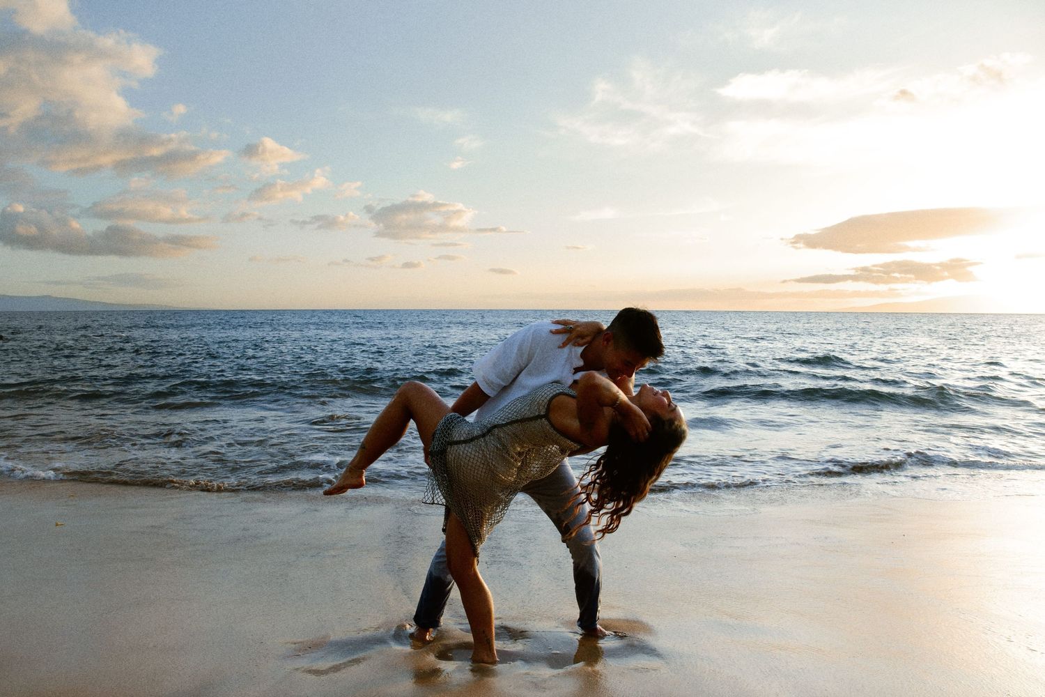 Couple dancing romantically on sandy beach at sunset with ocean in background.
