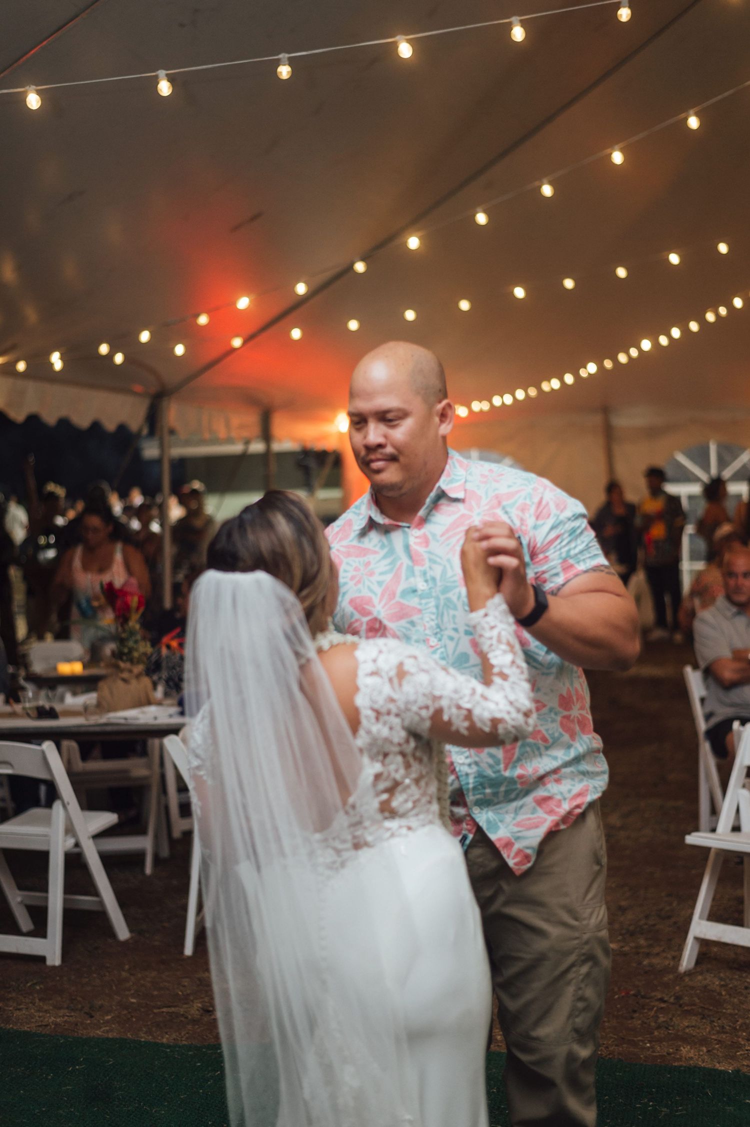 Bride and groom share a romantic first dance under string lights in a elegant wedding reception tent.
