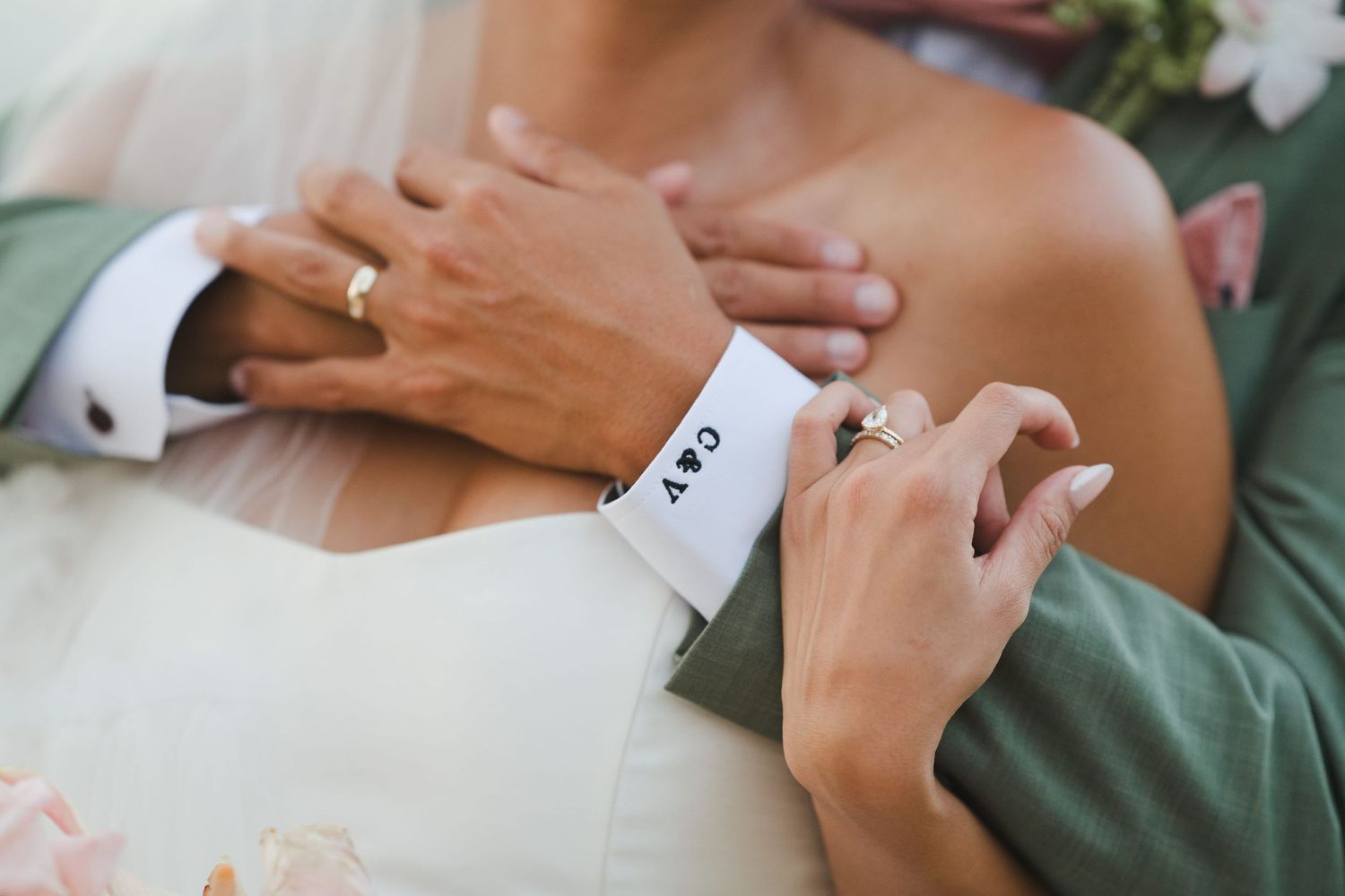 Close-up of groom's monogrammed cufflinks with bride's hands during wedding ceremony.