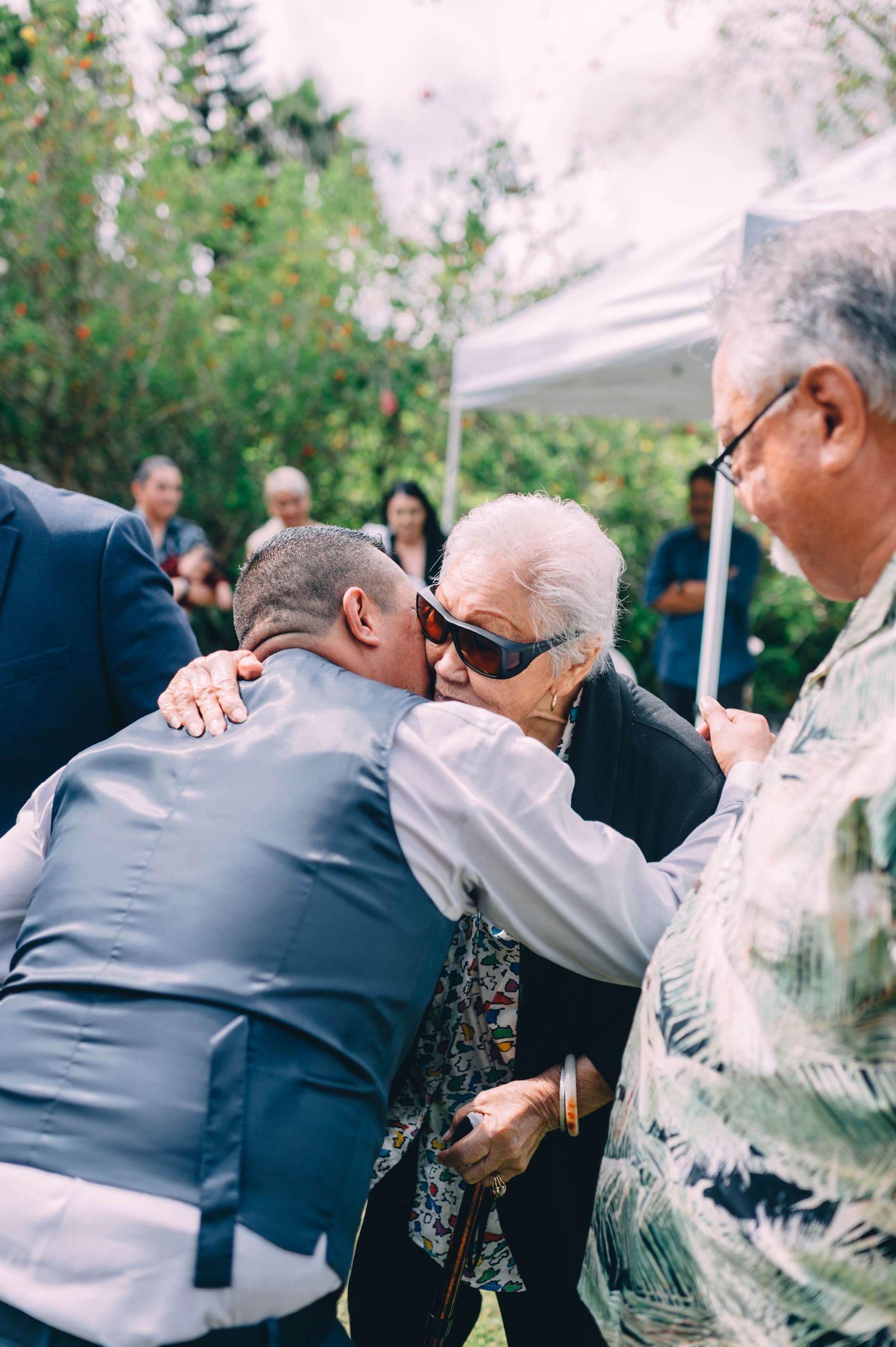Wedding guests share emotional embraces during an outdoor reception.