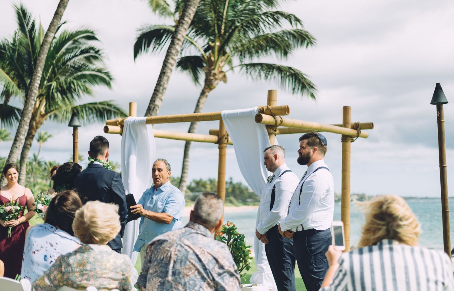 Beachfront wedding ceremony setup with bamboo arch and palm trees.