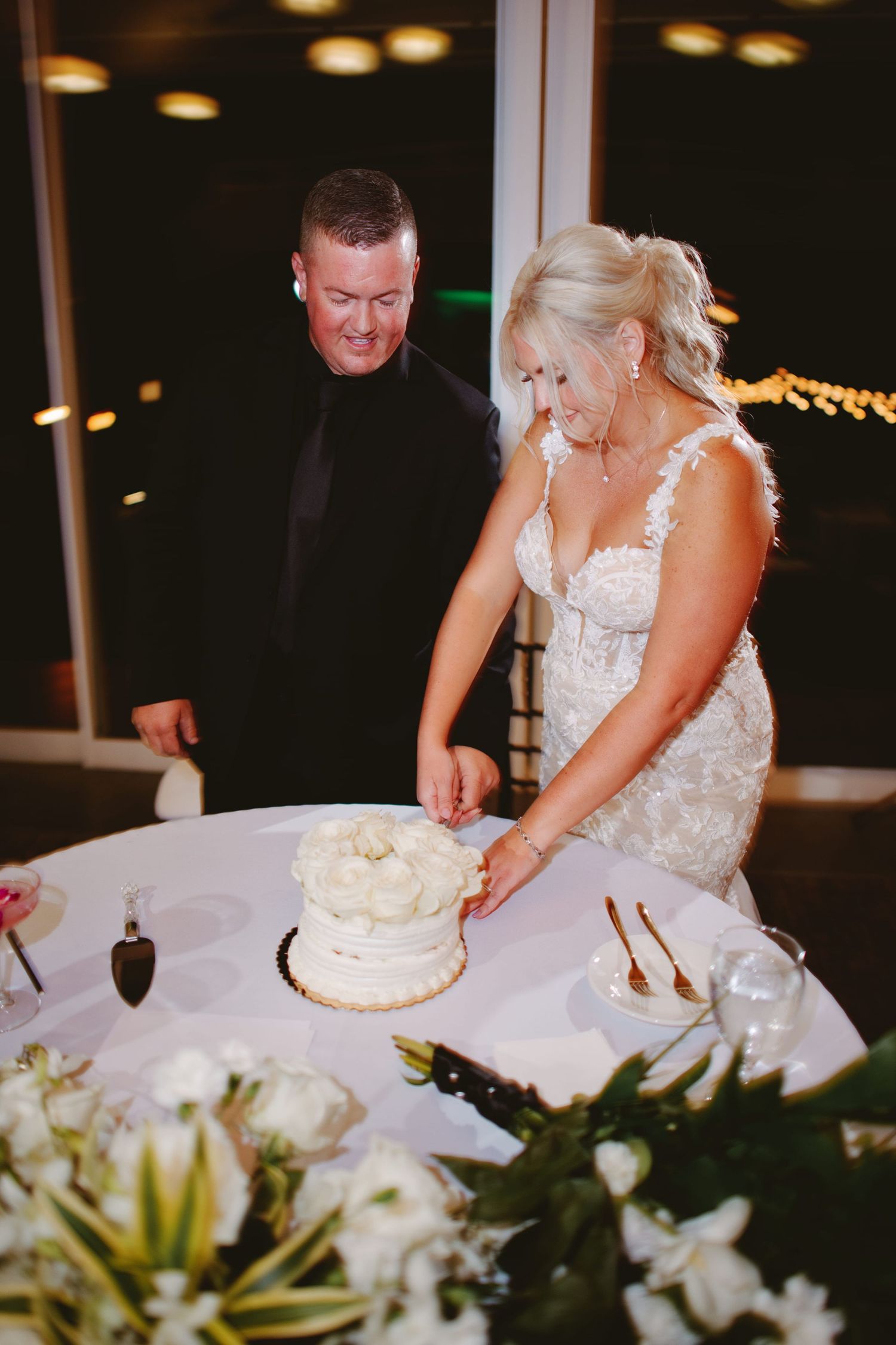Bride and groom cutting white wedding cake at elegant evening reception venue.