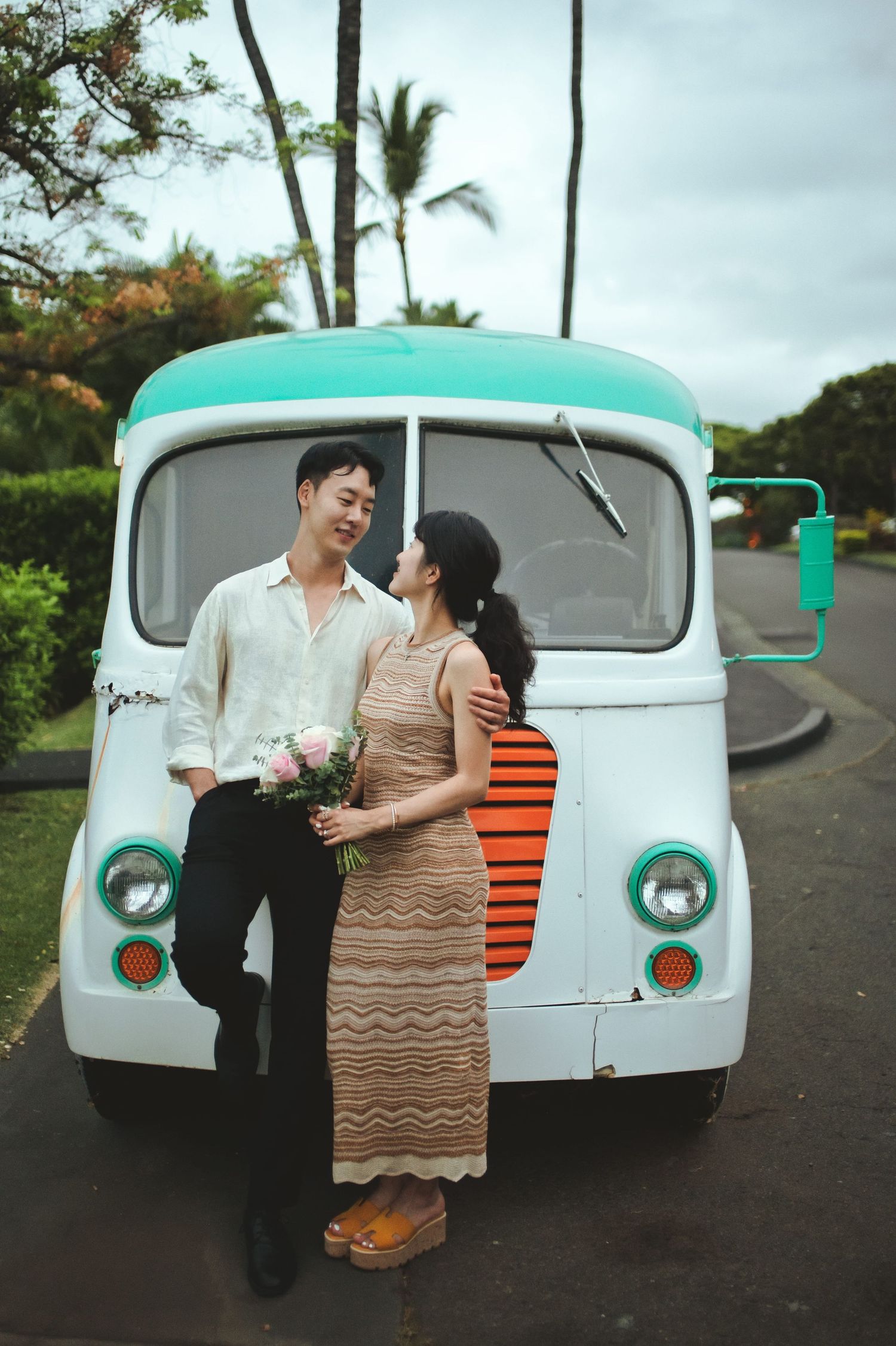 Couple posing in front of a vintage mint and white food truck, woman holding pink flowers, tropical setting at Hotel Wailea.