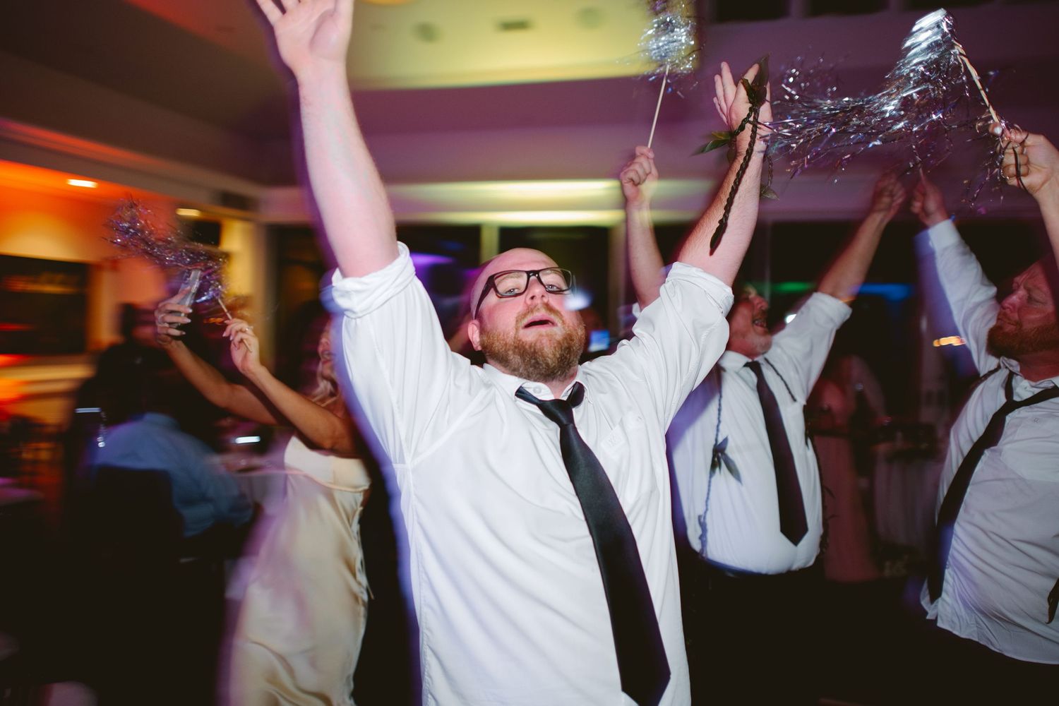 Excited wedding guest celebrates on the dance floor with arms raised at a lively reception party.