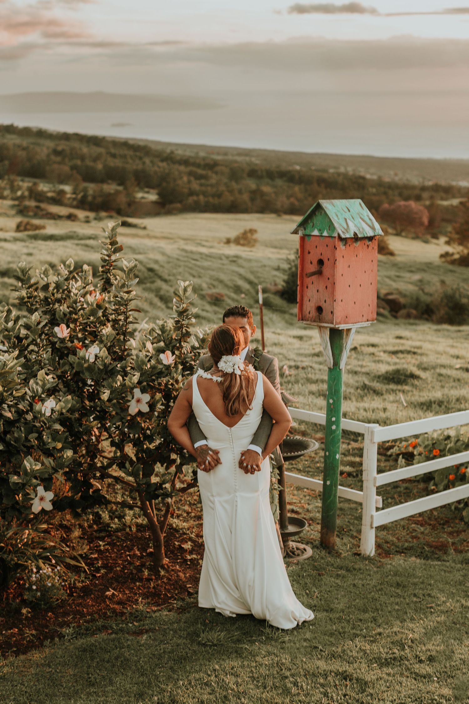 White dress flowing in the golden sunset light on a grassy hilltop with rustic mailboxes and fencing.