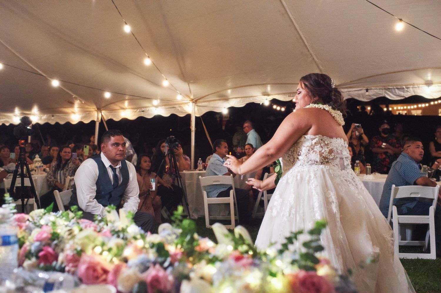 A bride in a lace wedding dress dances at her reception under a tent with string lights.